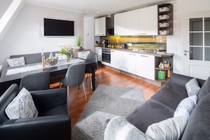 Une cuisine moderne avec des meubles blancs, une cuisinière noire et un plan de travail en bois. On y trouve également un coin repas avec un canapé gris et une table entourée de chaises.