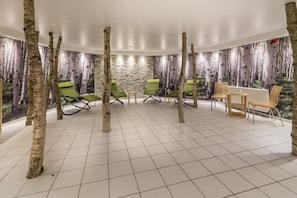 Une pièce avec des colonnes en bouleau, des fauteuils verts, une table en bois et un mur en pierre.