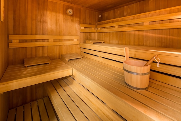 Un sauna avec des bancs en bois, un seau en bois et une horloge fixée au mur.