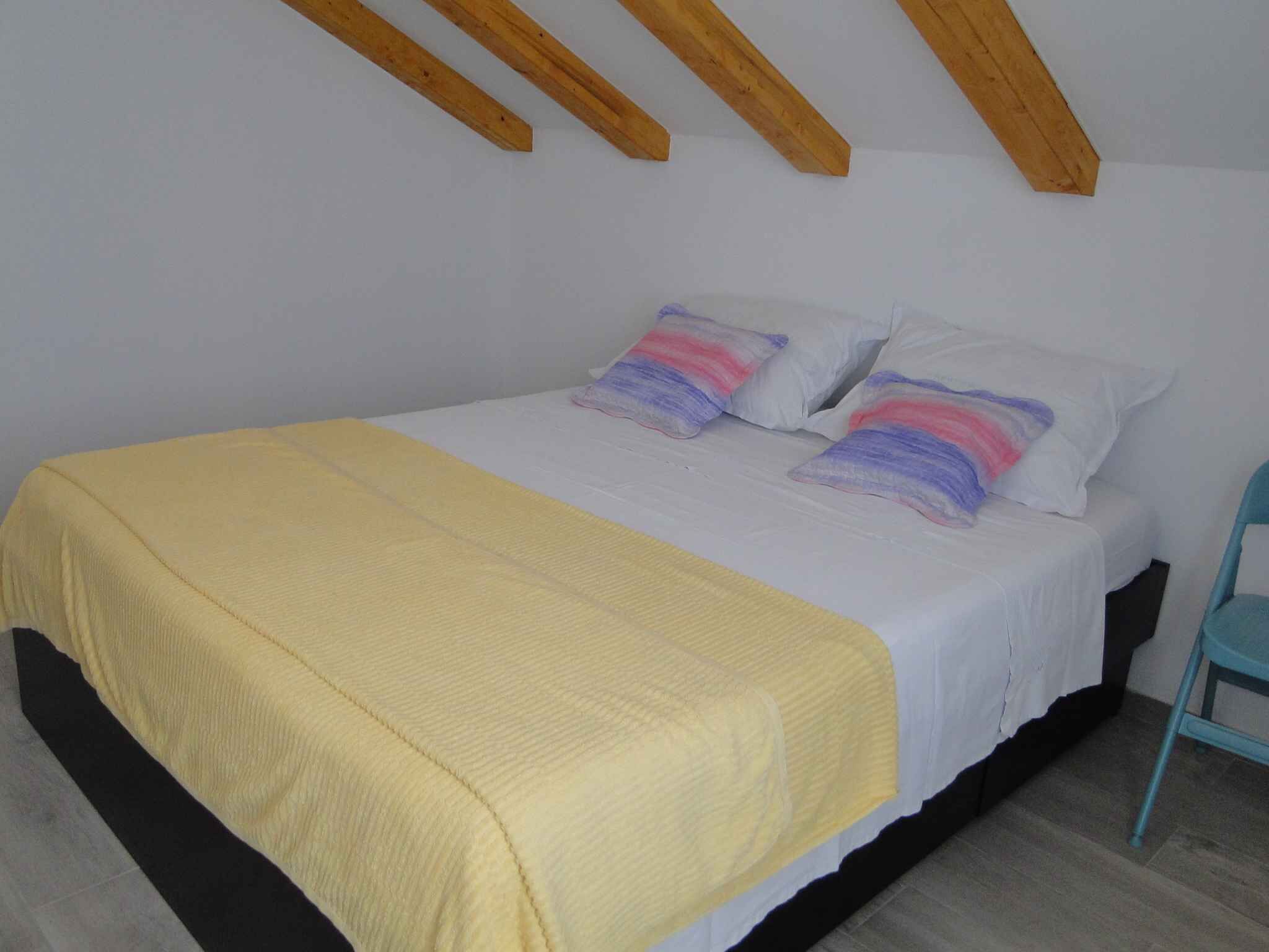 Una cama individual con una manta amarilla, ropa de cama blanca y dos almohadas con diseños pastel.