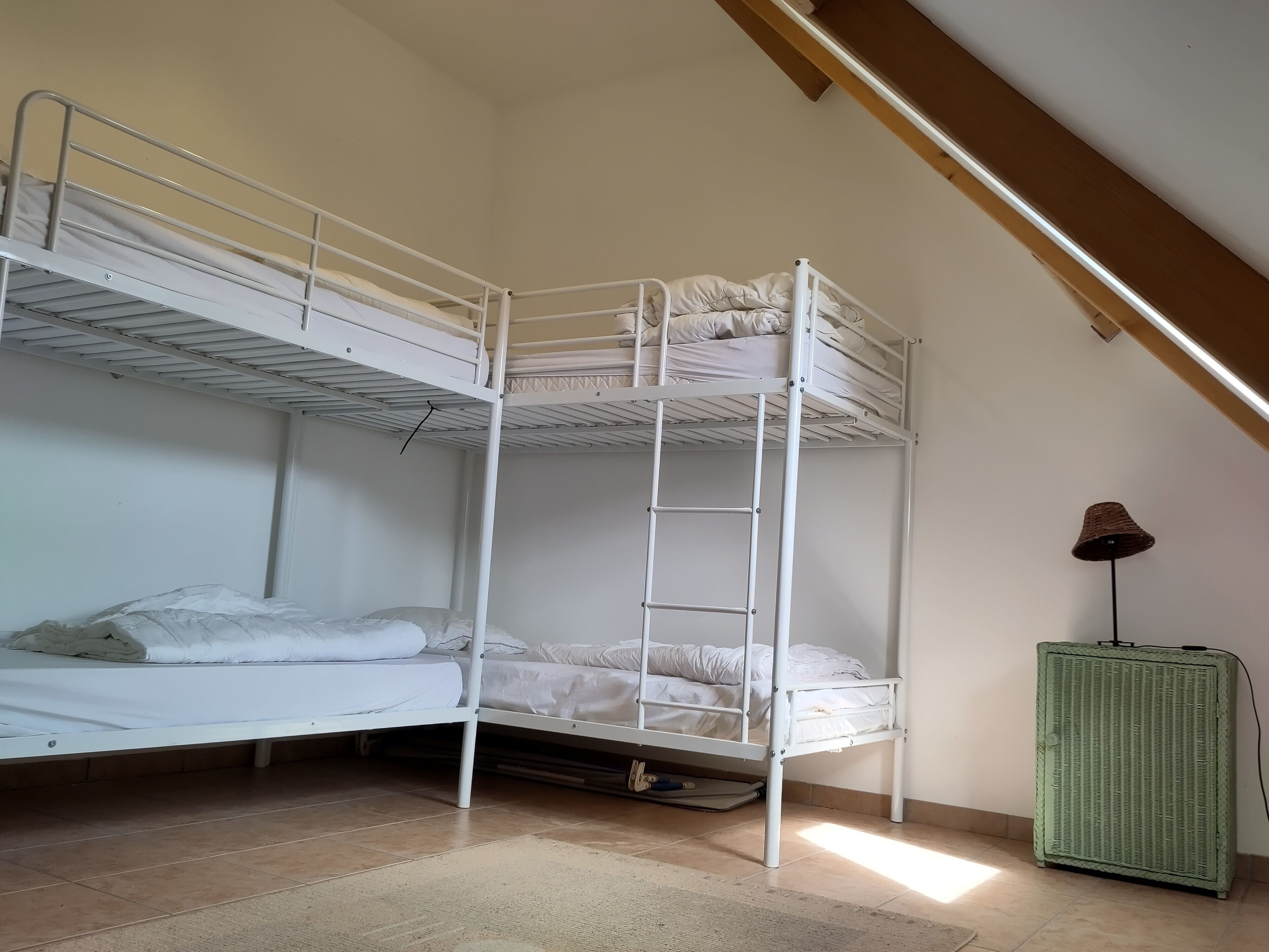 Une chambre avec un lit superposé, une échelle, un radiateur vert et une lampe.
