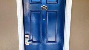 Puerta azul con placa de identificación, timbre y felpudo negro con la palabra BIENVENIDOS grabada.