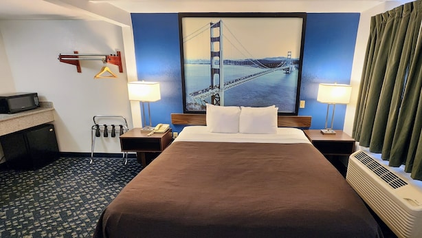 Habitación de hotel con una cama grande, dos mesitas de noche, un escritorio con microondas, un perchero y un cuadro del Puente Golden Gate.