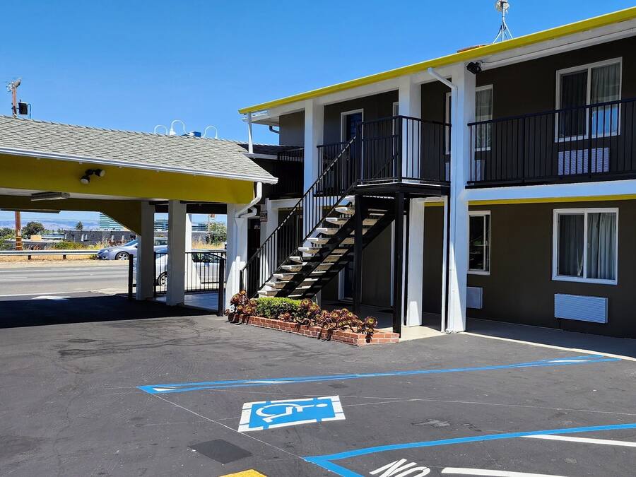 Ein Motel mit überdachtem Parkbereich, einer Treppe zum Obergeschoss und einem Schild für reservierte Parkplätze.