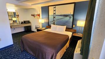 Quarto de hotel com uma cama grande, uma escrivaninha com computador, um espelho, um cabideiro e um quadro de uma ponte.