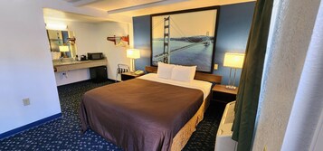 Quarto de hotel com uma cama grande, uma escrivaninha com computador, um espelho, um cabideiro e um quadro de uma ponte.