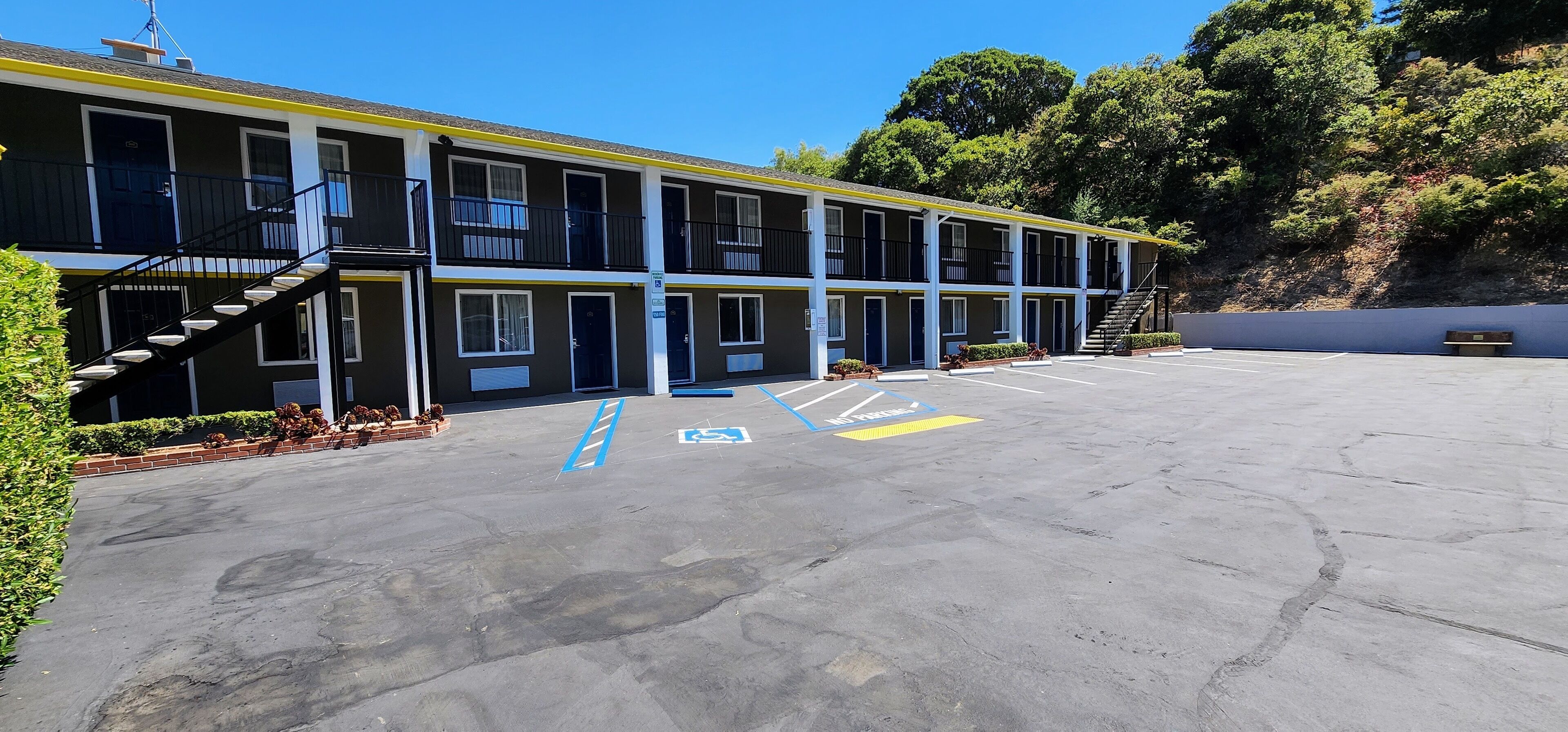 A motel with a parking lot, multiple units, and a staircase leading to the entrance.