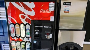 Máquina expendedora de Coca-Cola con diversas opciones de bebidas y un contenedor de reciclaje.