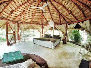 A spacious room with a thatched roof, a bed with pillows, a small table, and a chair. - Casa Picaflor (Las Terrenas)