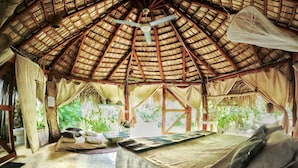 A thatched-roof hut with a bed, pillows, and a table. - Casa Picaflor (Las Terrenas)