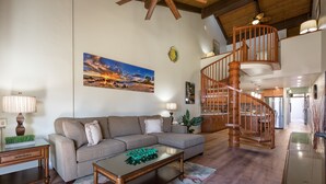 Amplia sala de estar con un sofá grande, una mesa de centro de madera y una escalera que lleva a un nivel superior.