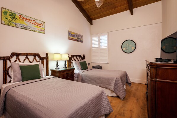 A bedroom with two beds, wooden headboards, a nightstand with a lamp, a dresser, and a world map on the wall. - REMODELED-KAMAOLE SANDS-BEAUTIFUL OCEAN VIEWS-AC-METICULOUS CLEANING (Kihei)