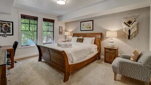 Ein Schlafzimmer mit einem hölzernen Bett, einem Schreibtisch, einem Sessel und einem Nachttisch mit einer Lampe.