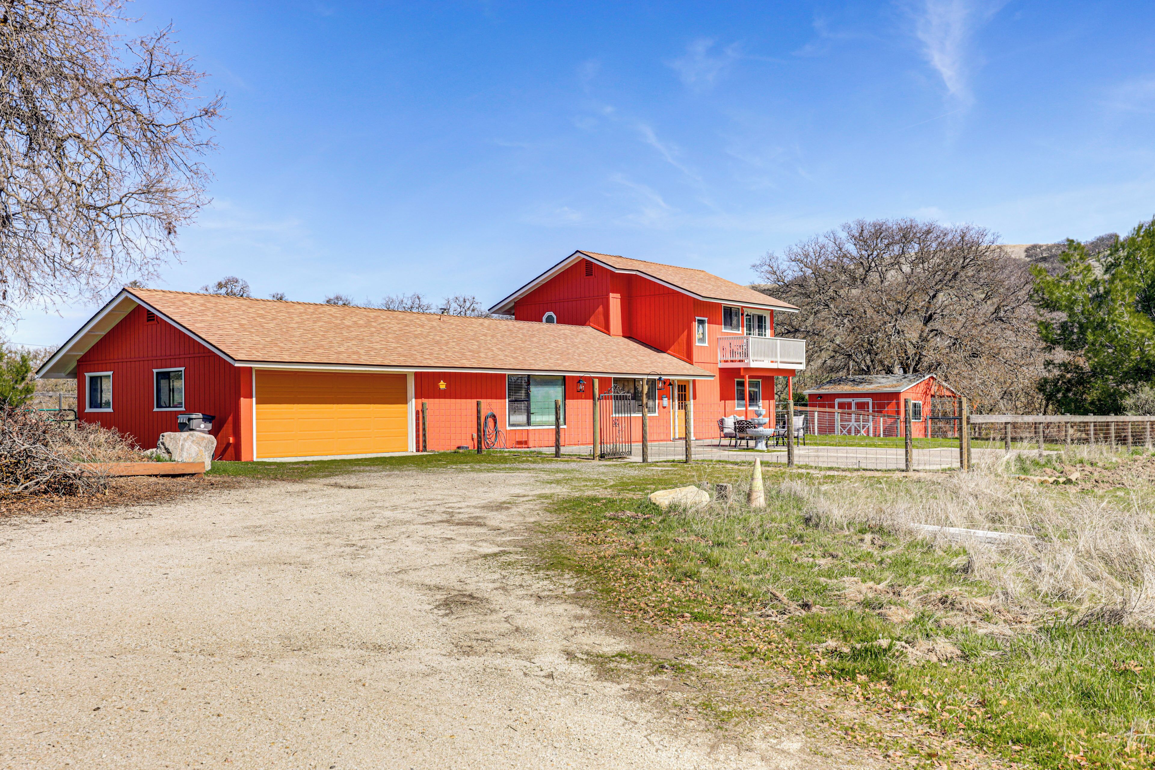 Une maison rouge à deux étages, avec un garage, une cour clôturée et un ciel d’un bleu éclatant.