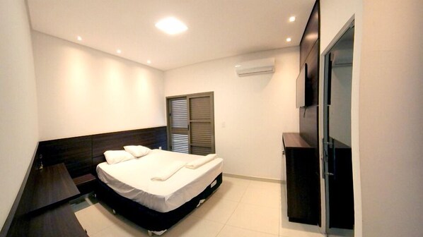 A modern bedroom with a bed, a dark headboard, a sliding door, and a built-in TV. - Recanto Rio Grande (São João Batista do Glória)