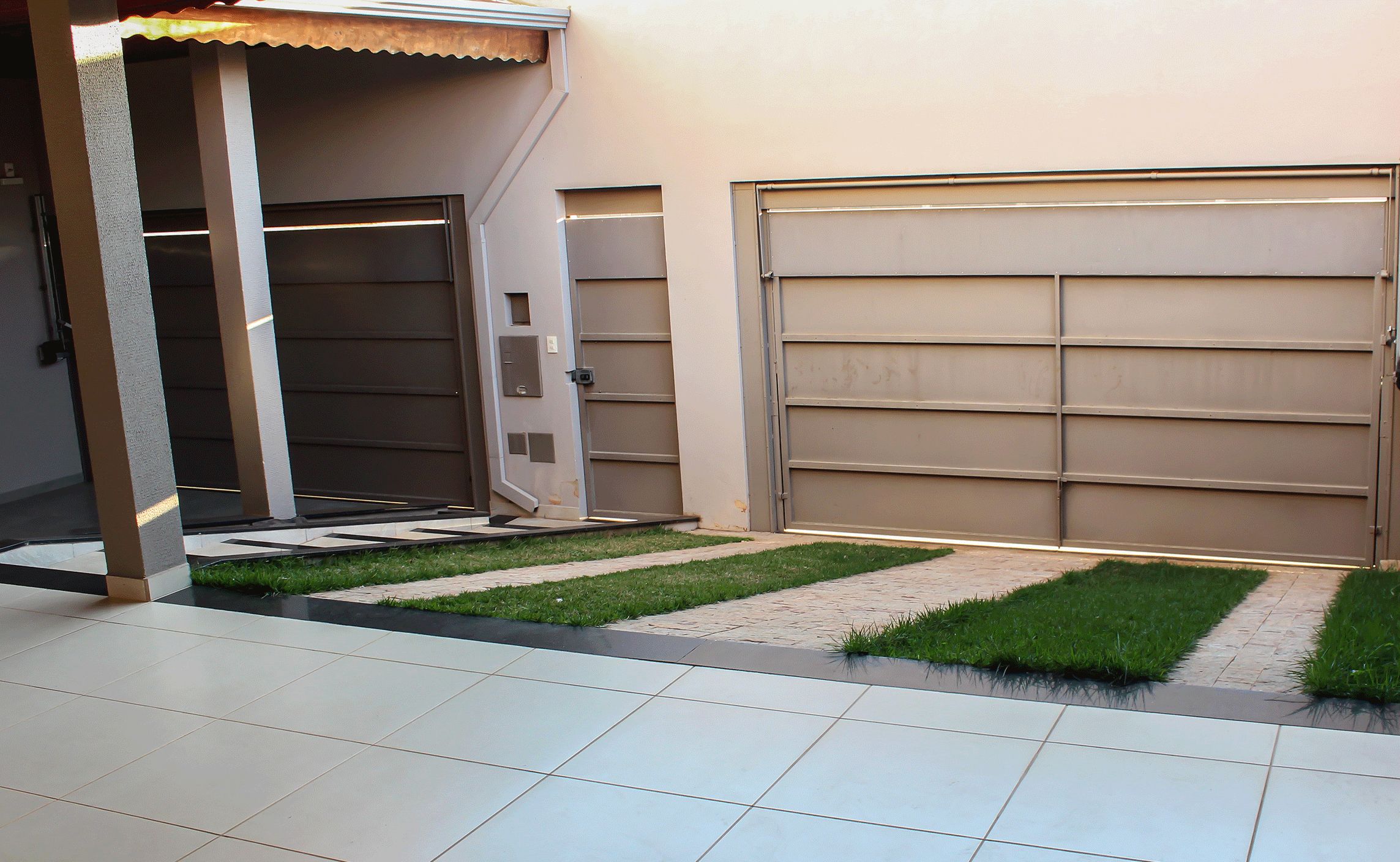Un garage moderne doté d’une grande porte fermée et d’un petit espace verdoyant à l’avant.