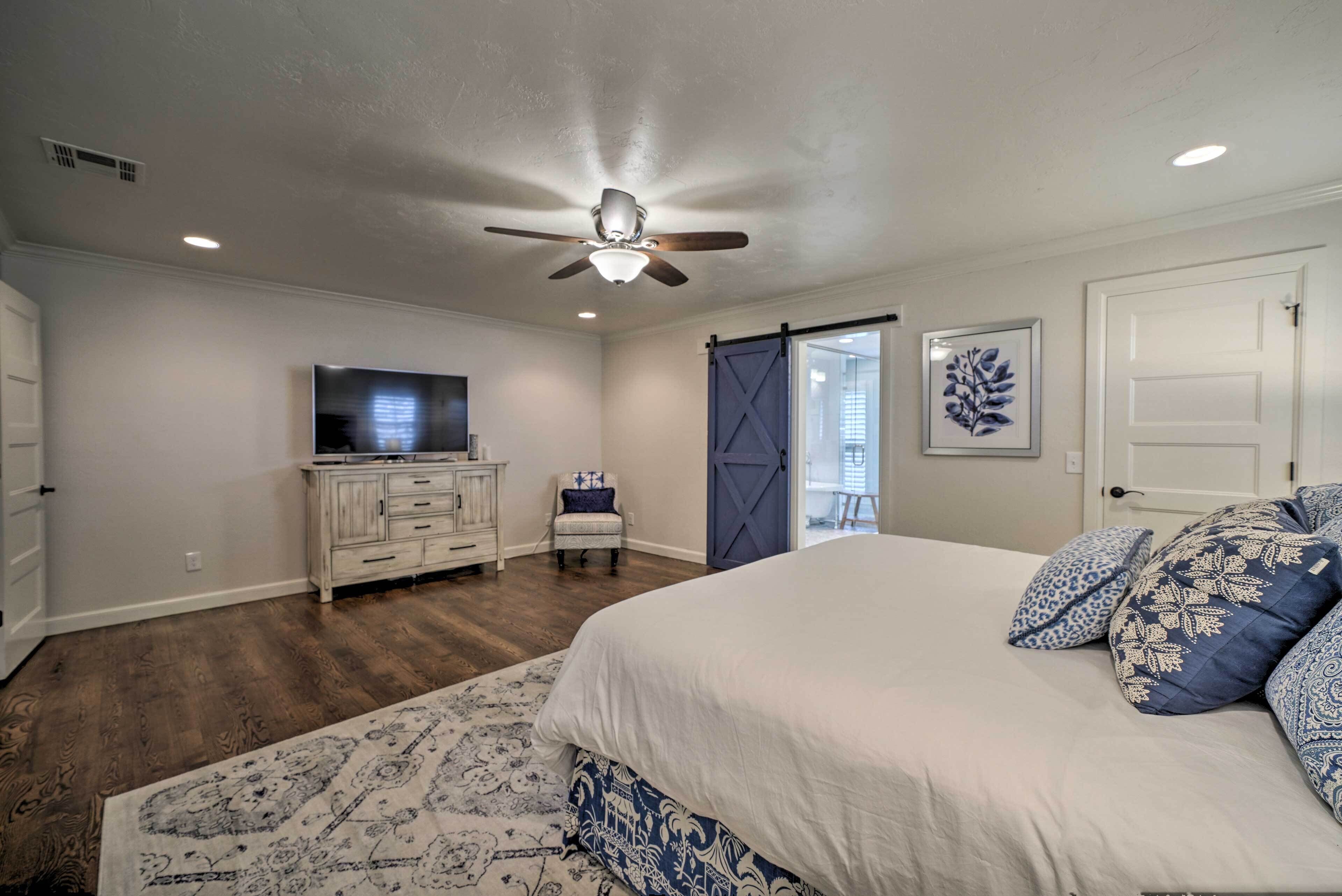 A bedroom with a bed, a ceiling fan, a dresser, a chair, a TV, and a door.