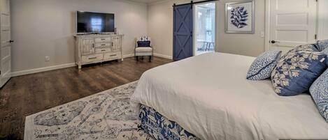 A bedroom with a bed, a ceiling fan, a dresser, a chair, a TV, and a door.