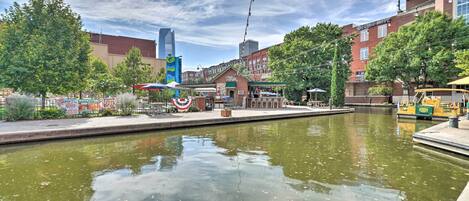 A riverside walkway with a brick building, a tall modern structure, and a boat dock.