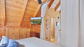 Dormitorio con paneles de madera, cama, cómoda, televisor montado en la pared y puerta que conduce a otra habitación.