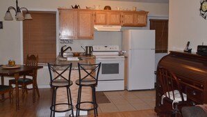 A compact kitchen with wooden cabinets, a white refrigerator, a stove, and two bar stools. - Peaceful Farm Atmosphere (Gainesboro)