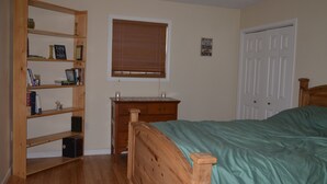 A bedroom with a wooden bed, a wooden nightstand, a bookshelf, a window with blinds, and a door. - Peaceful Farm Atmosphere (Gainesboro)
