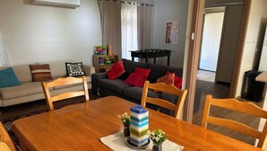 A dining area with a wooden table, chairs, a vase with flowers, and a sofa with cushions in the background.
