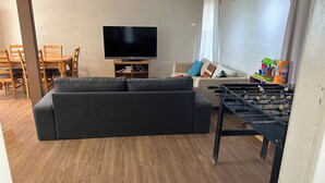 A living room with a sofa, a television, a dining table with chairs, and a foosball table.