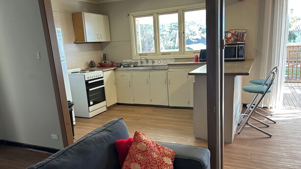 A kitchen with a stove, oven, and cabinets, a dining area with a table and chairs, and a sofa with cushions.
