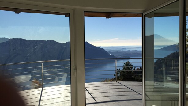 A room with a large sliding glass door leading to a balcony with a view of mountains and a lake. - Superb villa with panoramic view over Lake Maggiore (Pollino)