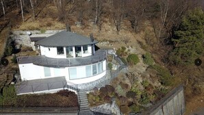A modern, single-story house with a curved roof, large windows, and a stone foundation. - Superb villa with panoramic view over Lake Maggiore (Pollino)