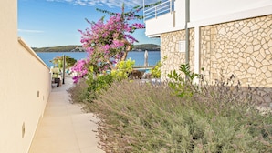 A narrow pathway leading to a building with a stone facade and a balcony overlooking a body of water. - EXCLUSIVE LOCATION BEACH APARTMENT "JAN"! NEW OPEN  SWIMMING POOL! (Trogir)