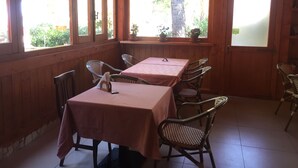 A wooden-paneled room with two tables and six chairs, large windows with a view of greenery, and a door with a frosted glass panel.