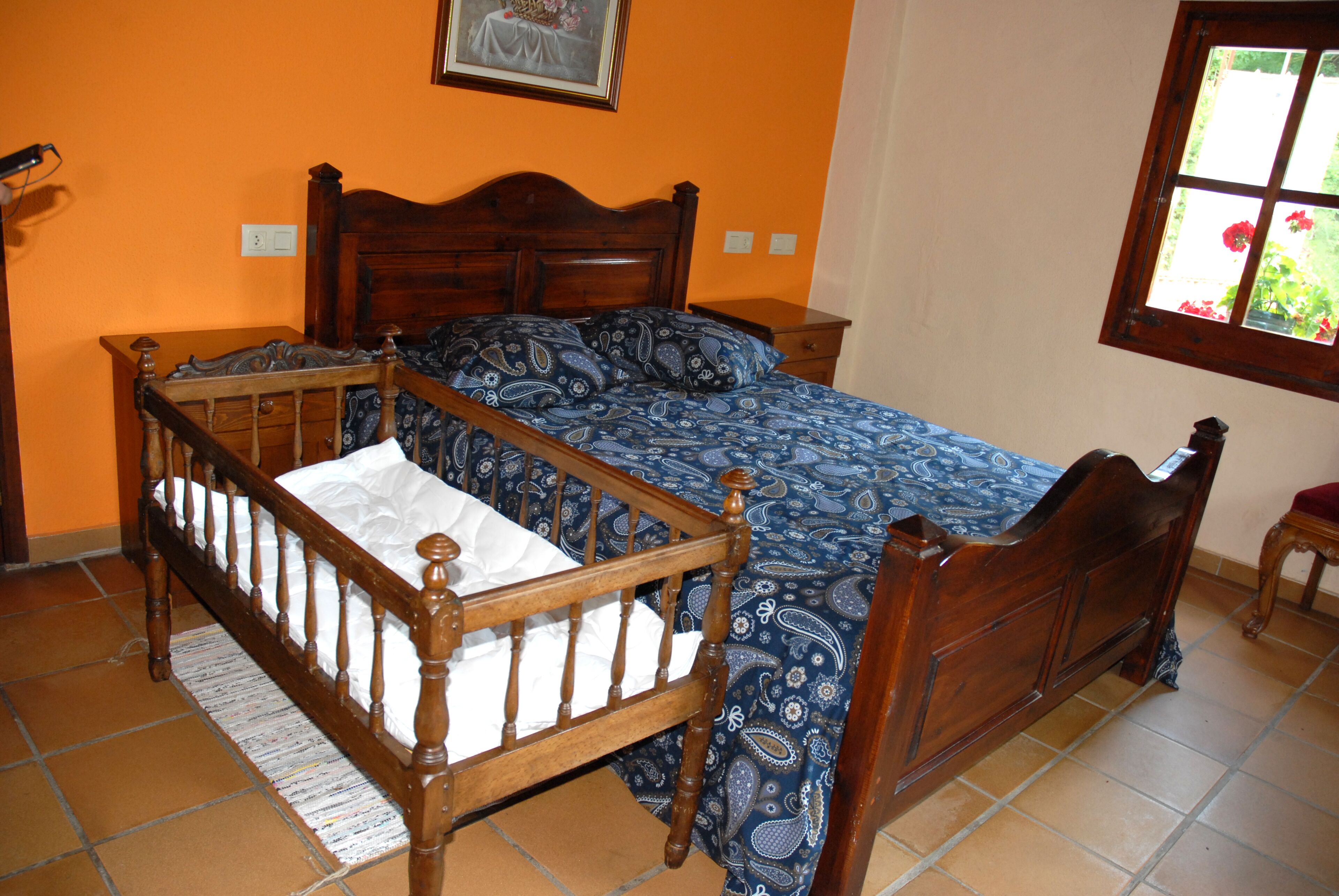 A bedroom with a wooden four-poster bed, a nightstand, and a window with a view of flowers.