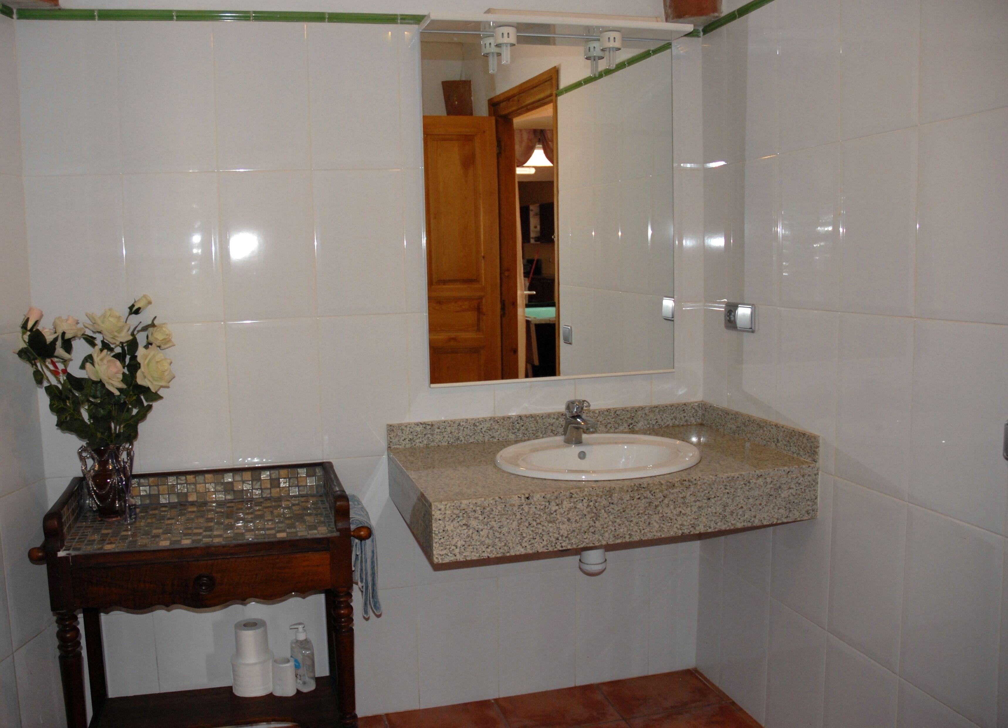 A bathroom with a sink, mirror, and a wooden vanity with a vase of flowers.