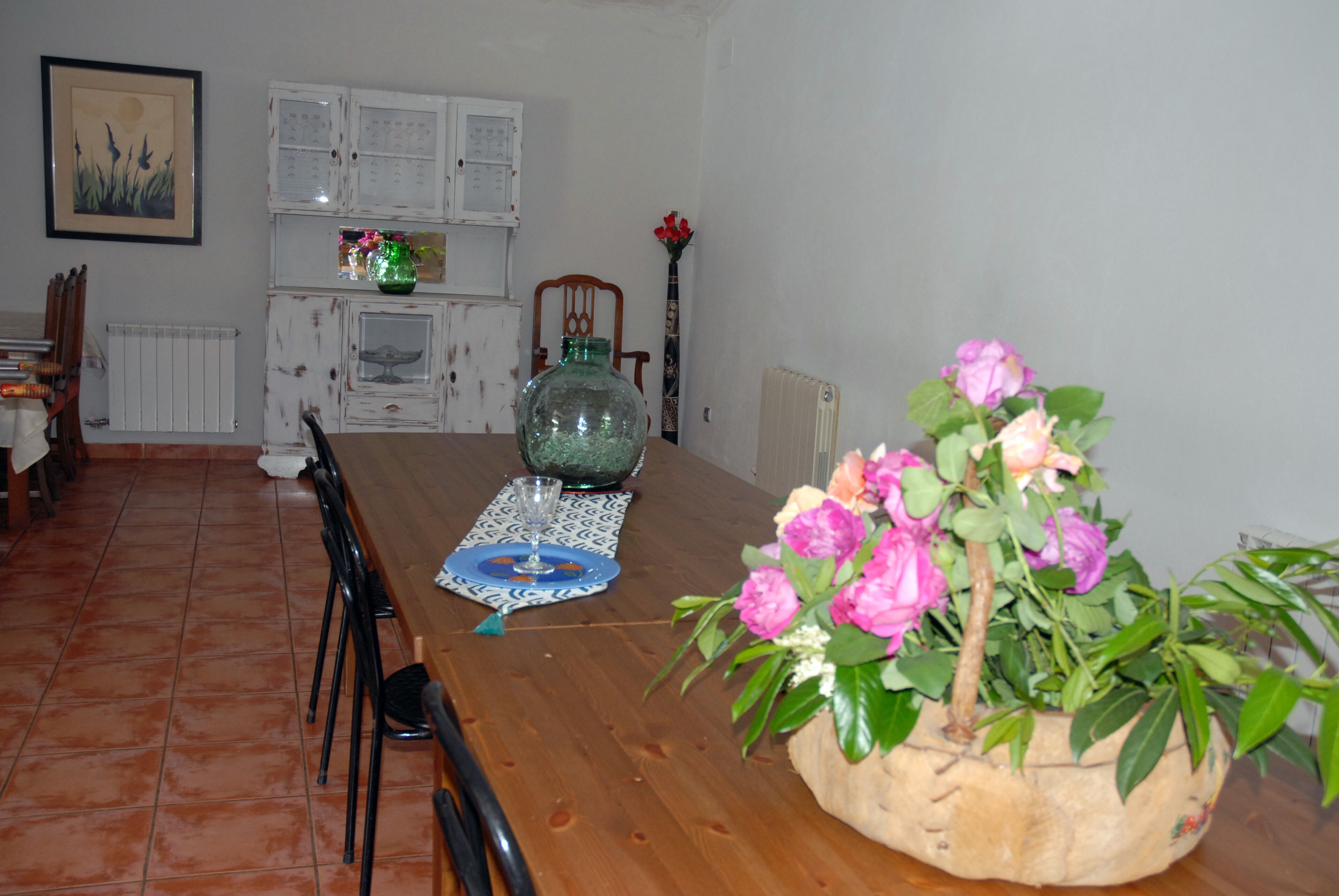 Un coin repas comprenant une table en bois, des chaises, un vase de fleurs et un meuble contenant des objets décoratifs.