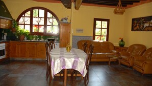 A dining area with a table set for six, surrounded by wooden chairs. There is a sofa with leather chairs in the background. - CANXAI THE RURAL TOURIST HOUSE OF LA GARROTXA PER ENJOY AMB QUI MÉS ESTIMES (La vall de Bianya)