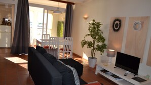 Ein Wohnzimmer mit einer schwarzen Couch, weißen Stühlen, einem Fernseher und einer Topfpflanze.
