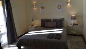 Ein ordentlich eingerichtetes Schlafzimmer mit einem Bett, Kissen, einem Nachttisch mit Lampe und Wandbildern.
