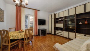 Un coin repas avec une table dressée pour quatre personnes, un téléviseur fixé au mur et un canapé au premier plan.