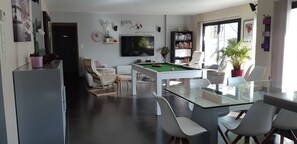 Un salon moderne avec une table de billard, des sièges confortables, une bibliothèque et une grande fenêtre.
