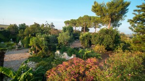A garden with various trees and shrubs, a stone pathway, and a statue. - Apartment with Pool and Park in Villa Oasi (Santa Barbara)