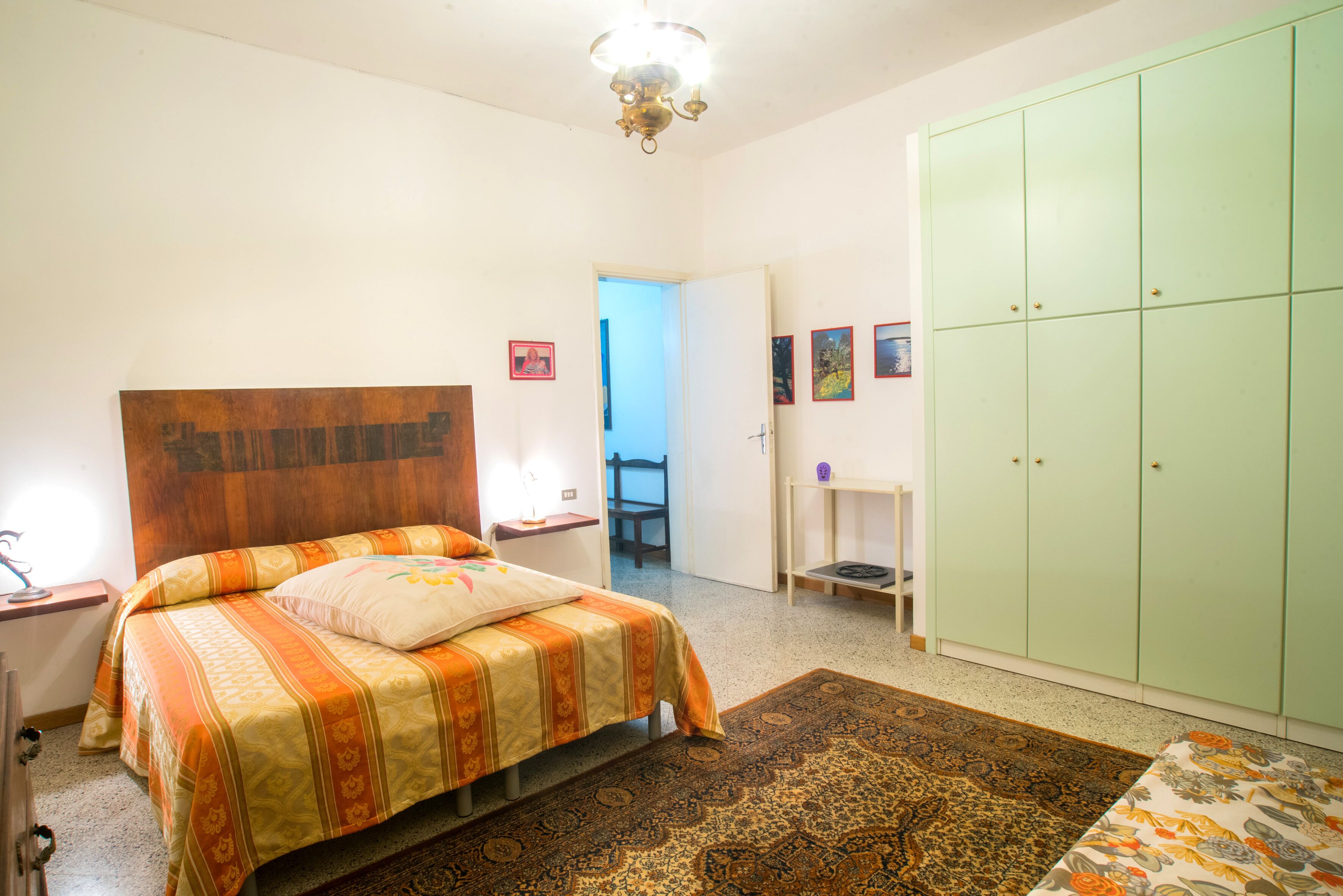 A bedroom with a bed, a nightstand, a wardrobe, and a door leading to another room.