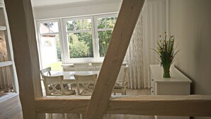 En matplats med ett träbord och stolar, ett vitt skåp med en vas med blommor och en utsikt över grönskan utanför genom stora fönster.