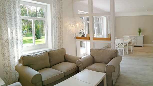 Ett modernt vardagsrum med en beige soffgrupp, ett vitt soffbord och en matplats med vita stolar och ett bord.