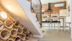 A staircase with a unique design of interlocking stone steps, leading to a kitchen area with white cabinetry, a wooden dining table, and a hanging light fixture.