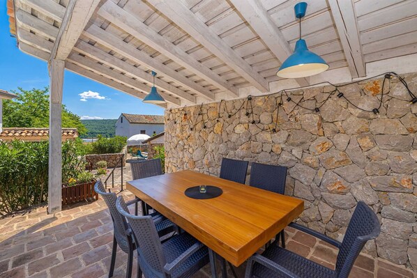 Eine Terrasse im Freien mit Steinmauer, Holztisch und Stühlen.