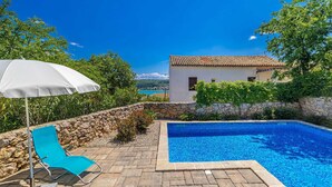 A swimming pool area with a stone wall, a white building, and a clear blue sky.