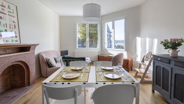 A dining area with a brick fireplace, a table set for two, and a view of the outdoors through large windows. - Le Timonier - Two Bedroom Apartment, Sleeps 4 (Saint-Malo)
