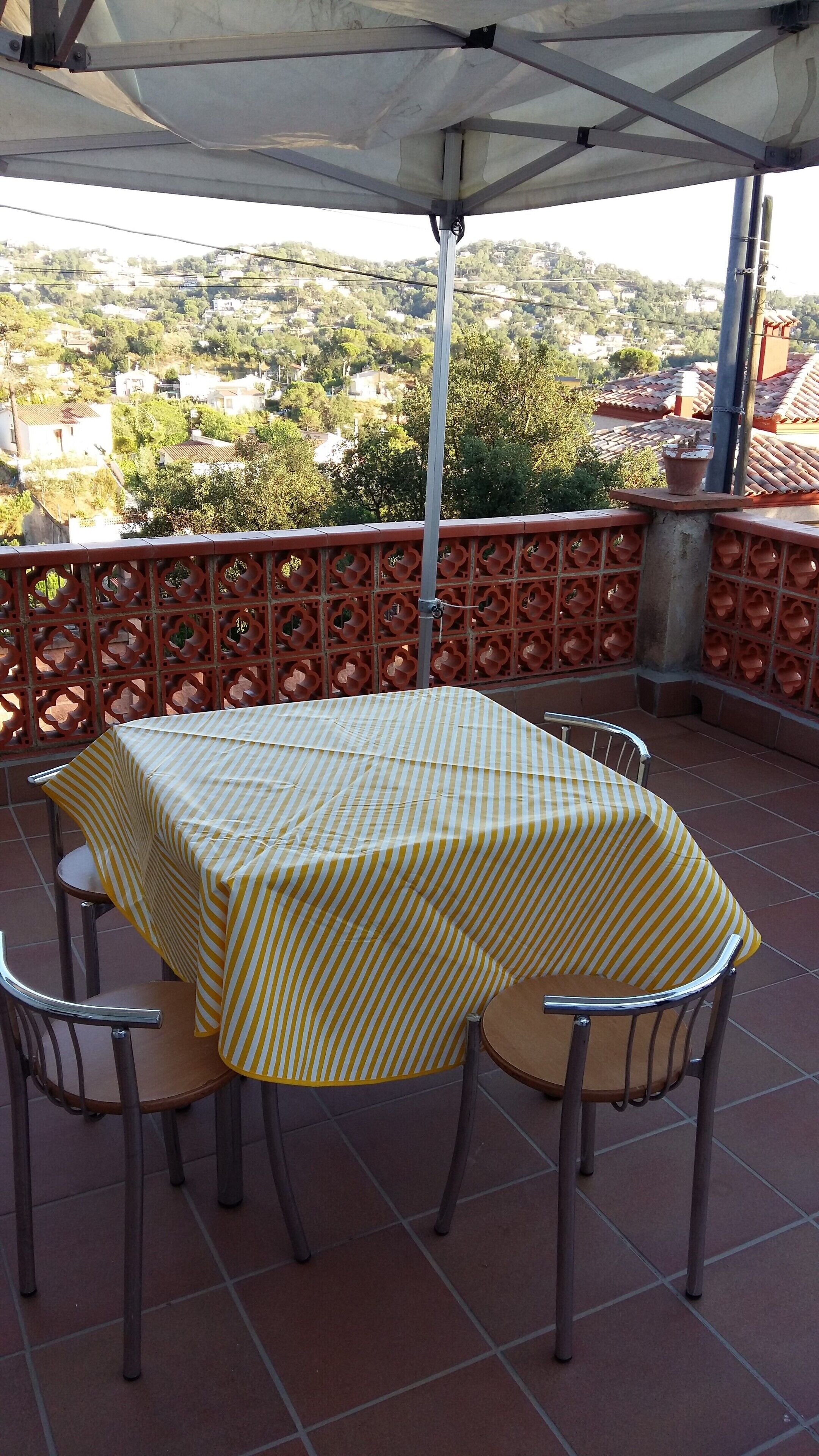 A terrace with a table and chairs, a view of a town, and a decorative fence.
